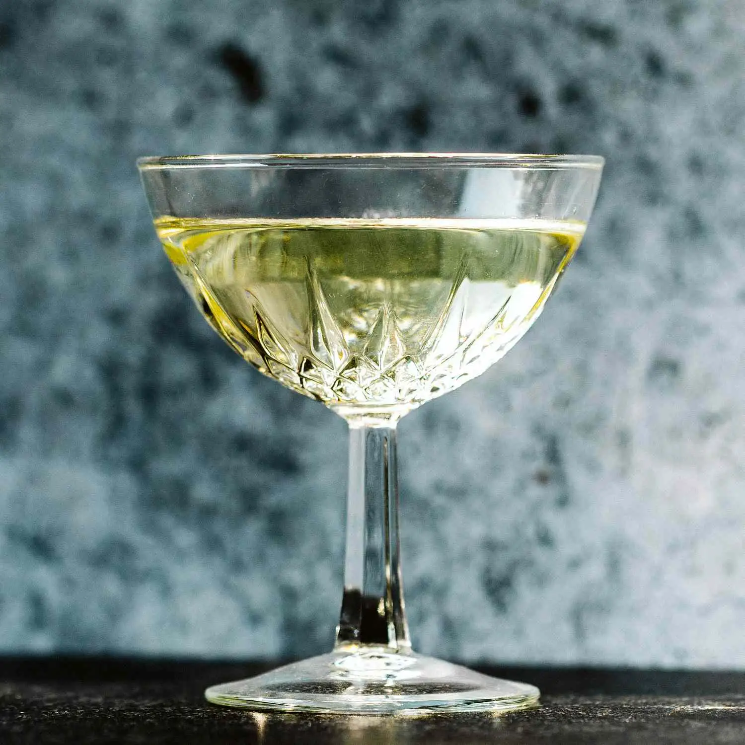 Polar Bear cocktail, pale yellow, in engraved coupe glass on grey textured background