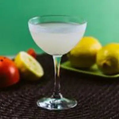 An elegantly curved coupe with a sugared rim is filled with a lightly a bright Lemon Drop. Surrounding it are a variety of lemons, as well as a red lemon squeezer
