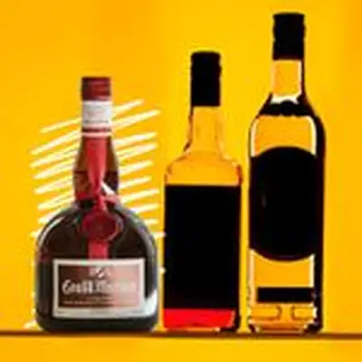 A stout Grand Marnier bottle sits on a yellow background. Next to it are other liquor bottles, their labels in shadow