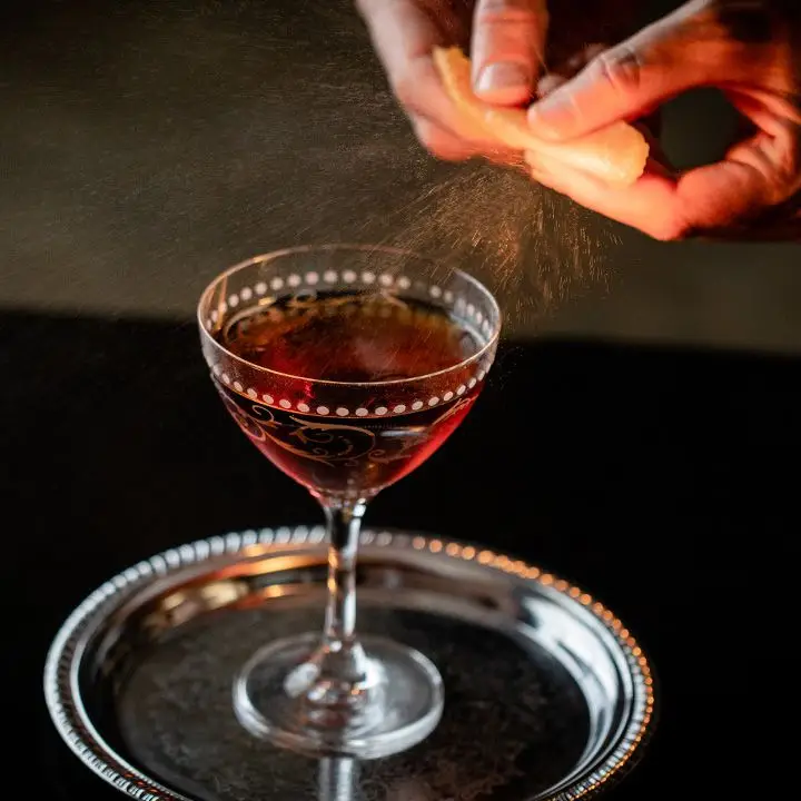 Hands express orange peel oils over the top of the Longshoreman cocktail