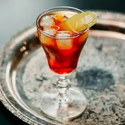 bright-red picon punch cocktail in an Irish Coffee glass over ice, garnished with a lemon peel and served on a round silver tray