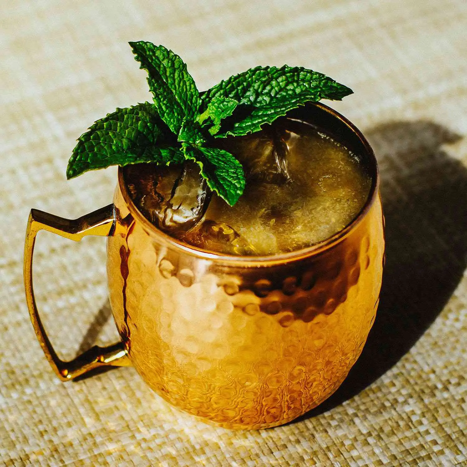 Kentucky Mule served in a copper mug and topped with a mint sprig garnish, served on a straw mat
