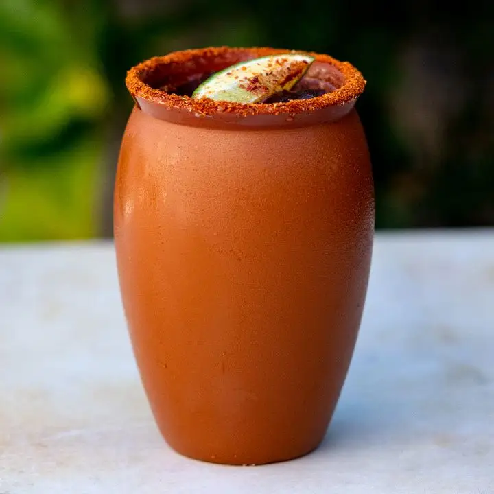 Cantarito cocktail served in clay jug with tajin rim and lime wedge