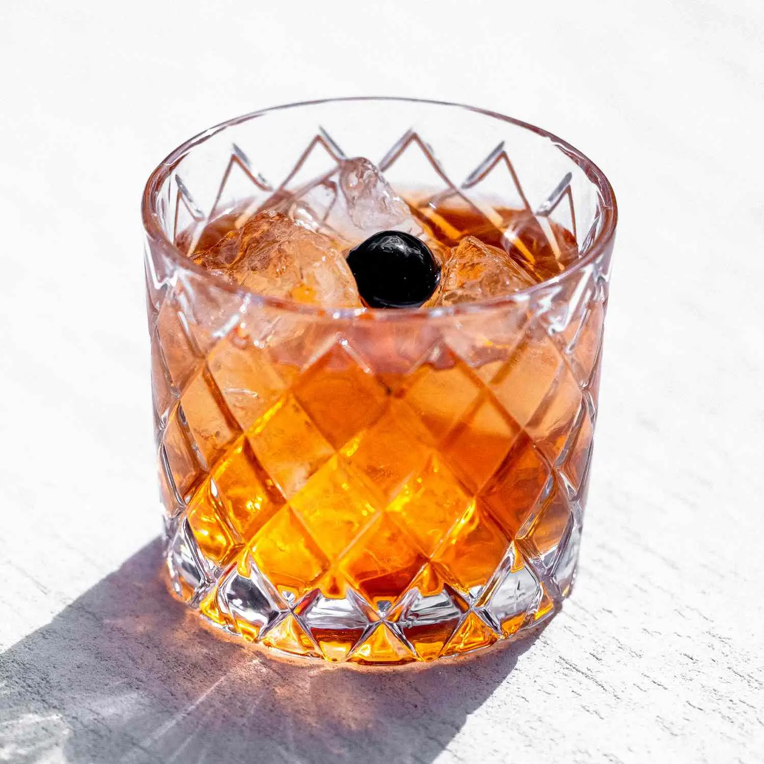 Anejo Old Fashioned served with ice in rocks glass, garnished with maraschino cherry and shot against textured white background