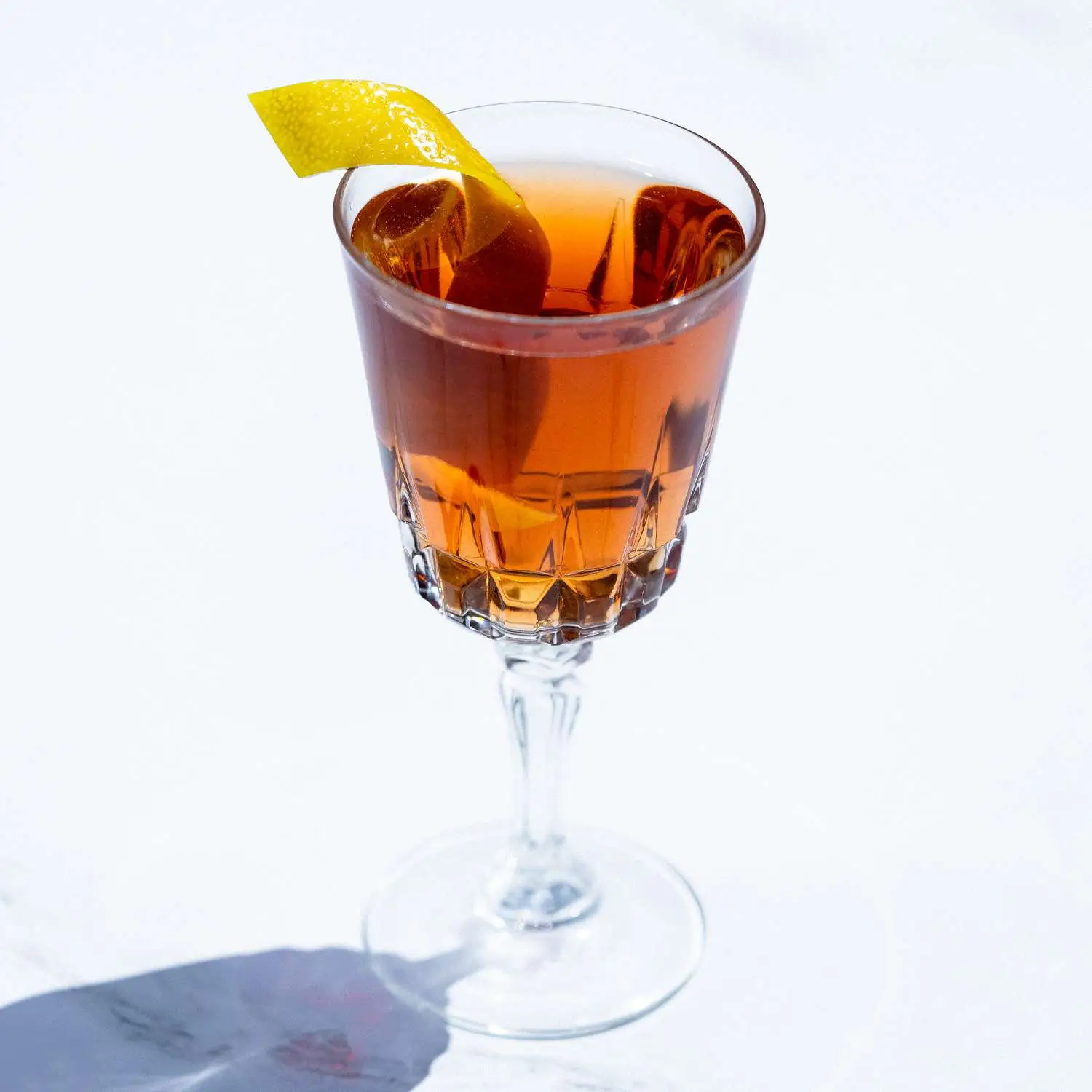 La Perla cocktail garnished with lemon twist and shot against white background