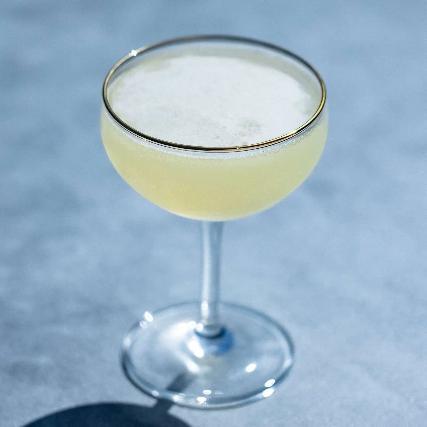 Tequila Daisy cocktail in gold-rimmed coupe glass, shot against gray background
