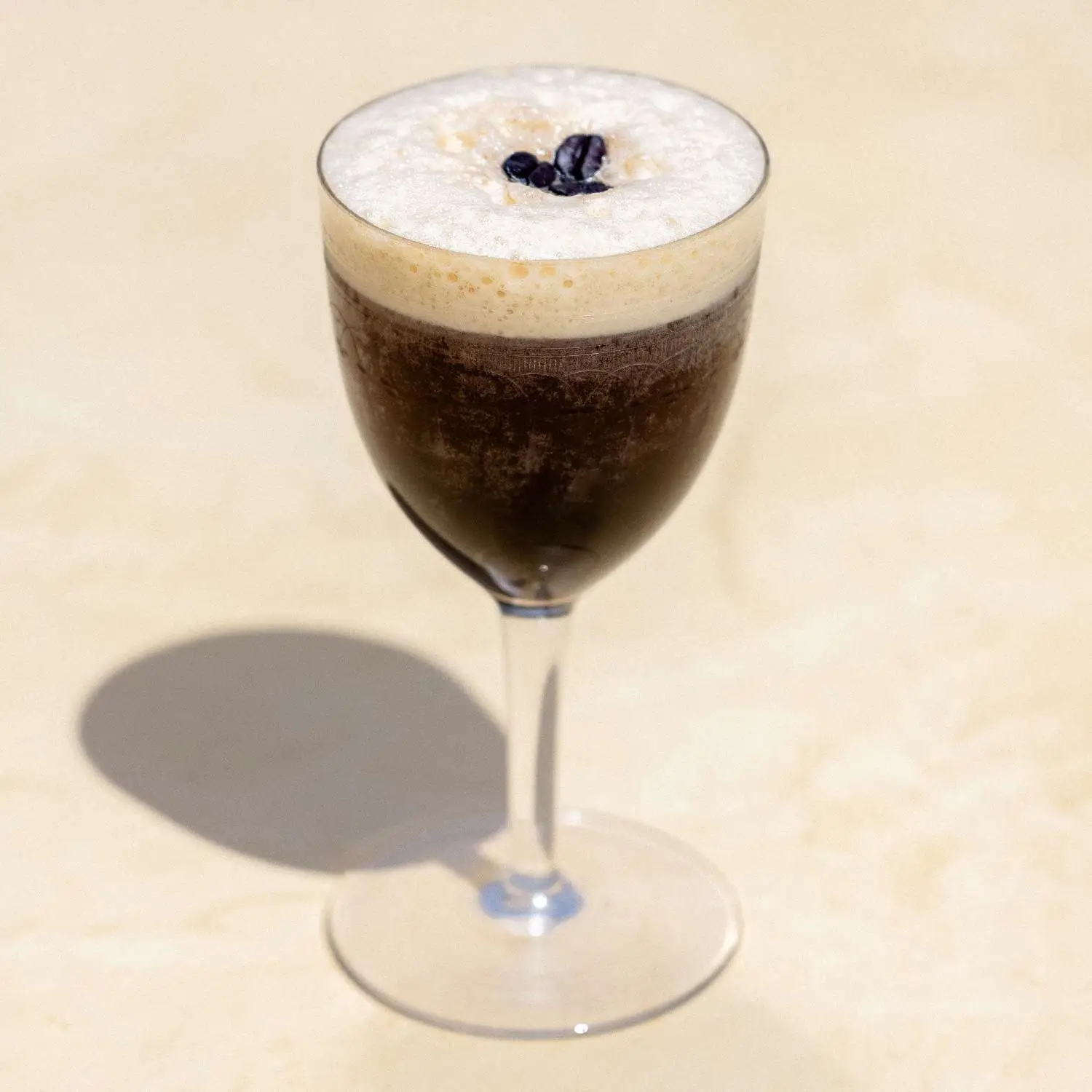 Tequila Espresso Martini served in Nick and Nora glass with thick foam, garnished with three espresso beans and shot against tan background