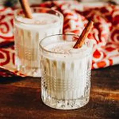 two eggnog cocktails with cinnamon sticks and nutmeg garnish