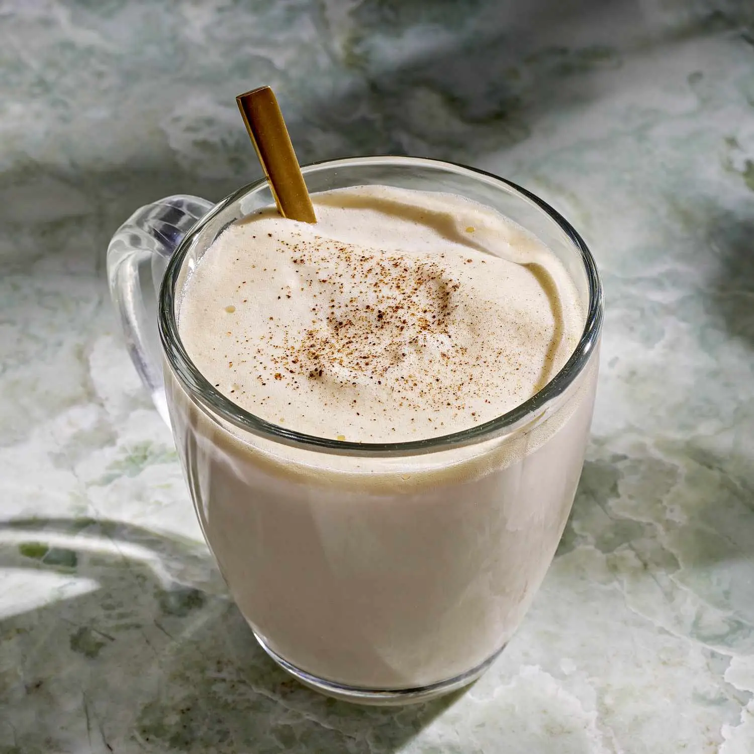 Tom & Jerry cocktail in clear coffee mug with metal spoon and dusting of ground clove, nutmeg, and allspice on top