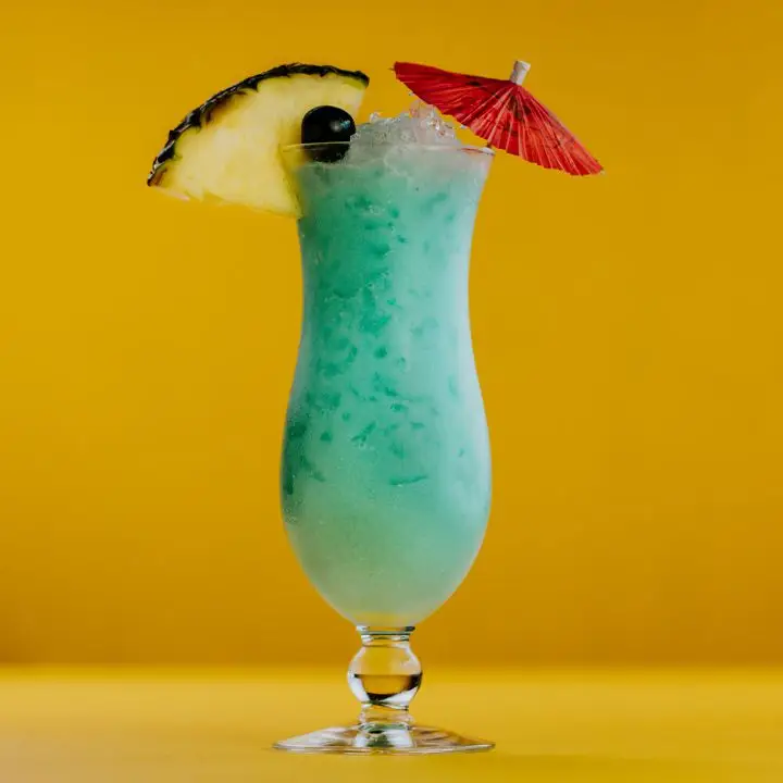 blue hawaiian cocktail with pineapple and umbrella garnish, set against a yellow background