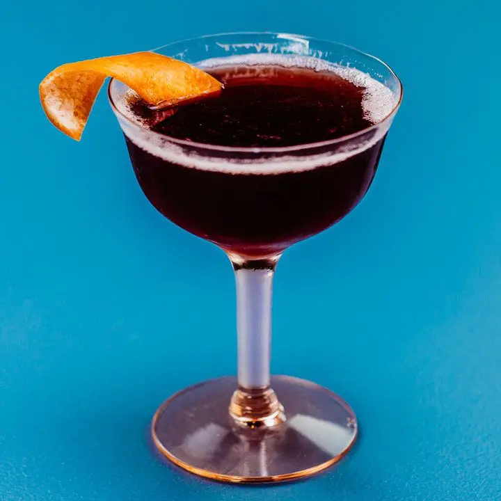 deep burgundy-colored Improved Dunlop cocktail in a coupe, with a grapefruit peel garnish