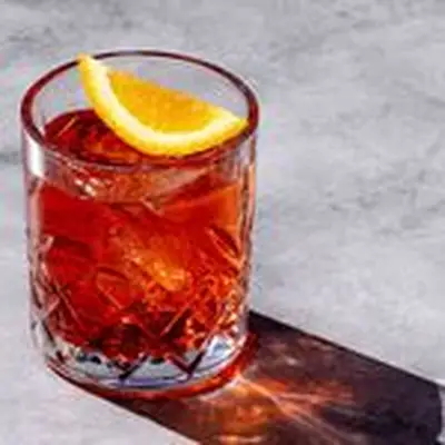 Vibrant red Mezcal Negroni in etched rocks glass on marble background, with orange garnish