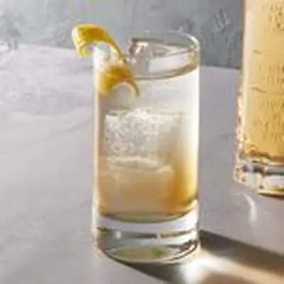 St-Germain cocktail in highball glass, with St-Germain measuring glass in the background holding extra spritz