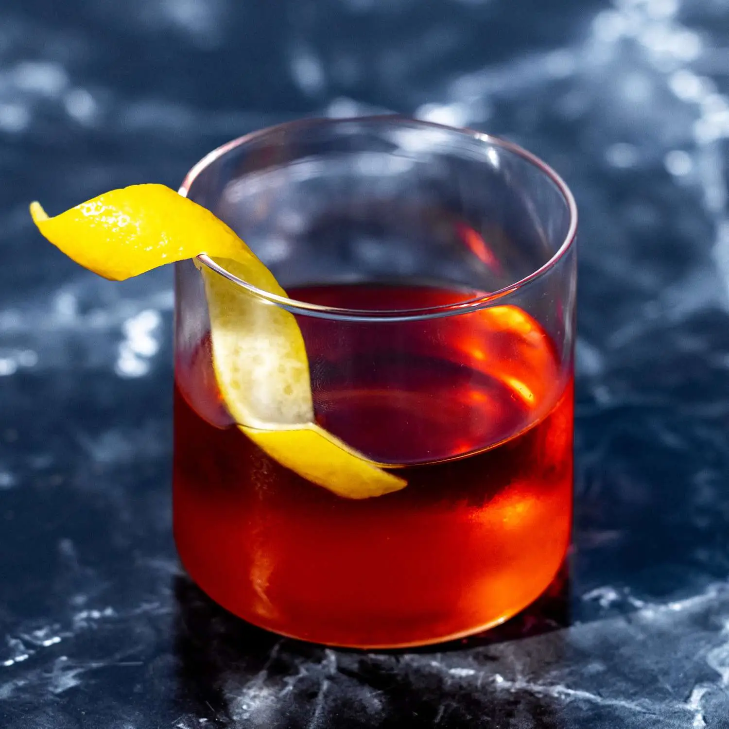 Sazerac, reddish brown, in rocks glass without ice, garnished with lemon twist, on a dark marble background