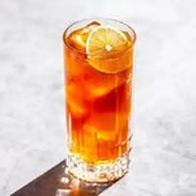 Dark and Stormy cocktail in a highball glass with lime wheel on top, photographed on light marble background