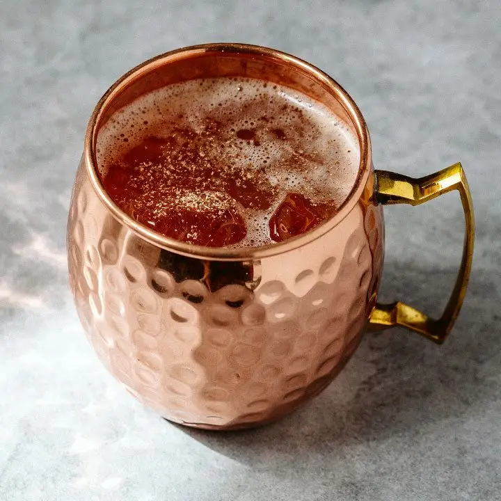 A hammered copper mug rests on a marble counter. Ice and a drink fill the cup, and it’s garnished with a dusting of nutmeg. 
