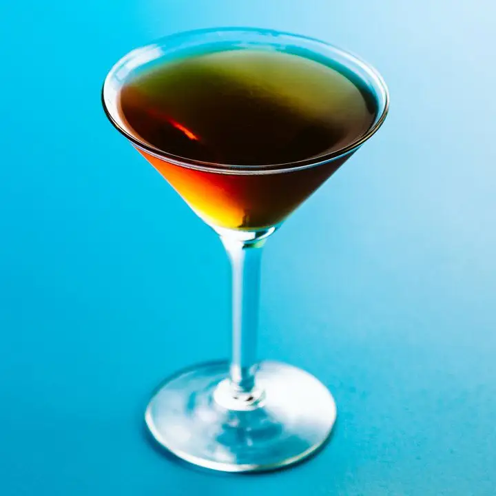 chartreuse manhattan cocktail in a cocktail glass, served on a blue backdrop