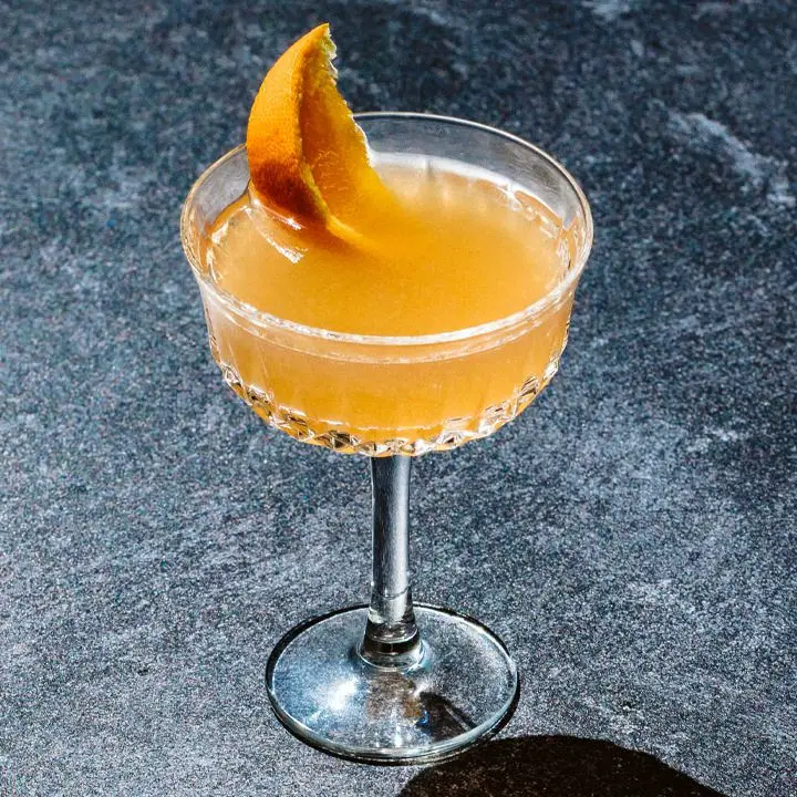 orange-colored Rum Rangoon cocktail in a cocktail glass, garnished with an orange wedge