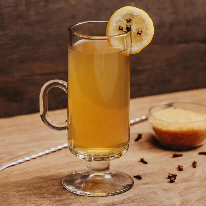 Hot Toddy cocktail in a glass mug with lemon wheel and cloves