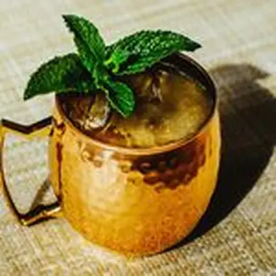 Kentucky Mule served in a copper mug and topped with a mint sprig garnish, served on a straw mat