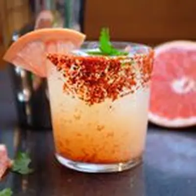 Vida Paloma cocktail in a chile piquin-rimmed rocks glass, garnished with a grapefruit wedge, jalapeño round and cilantro