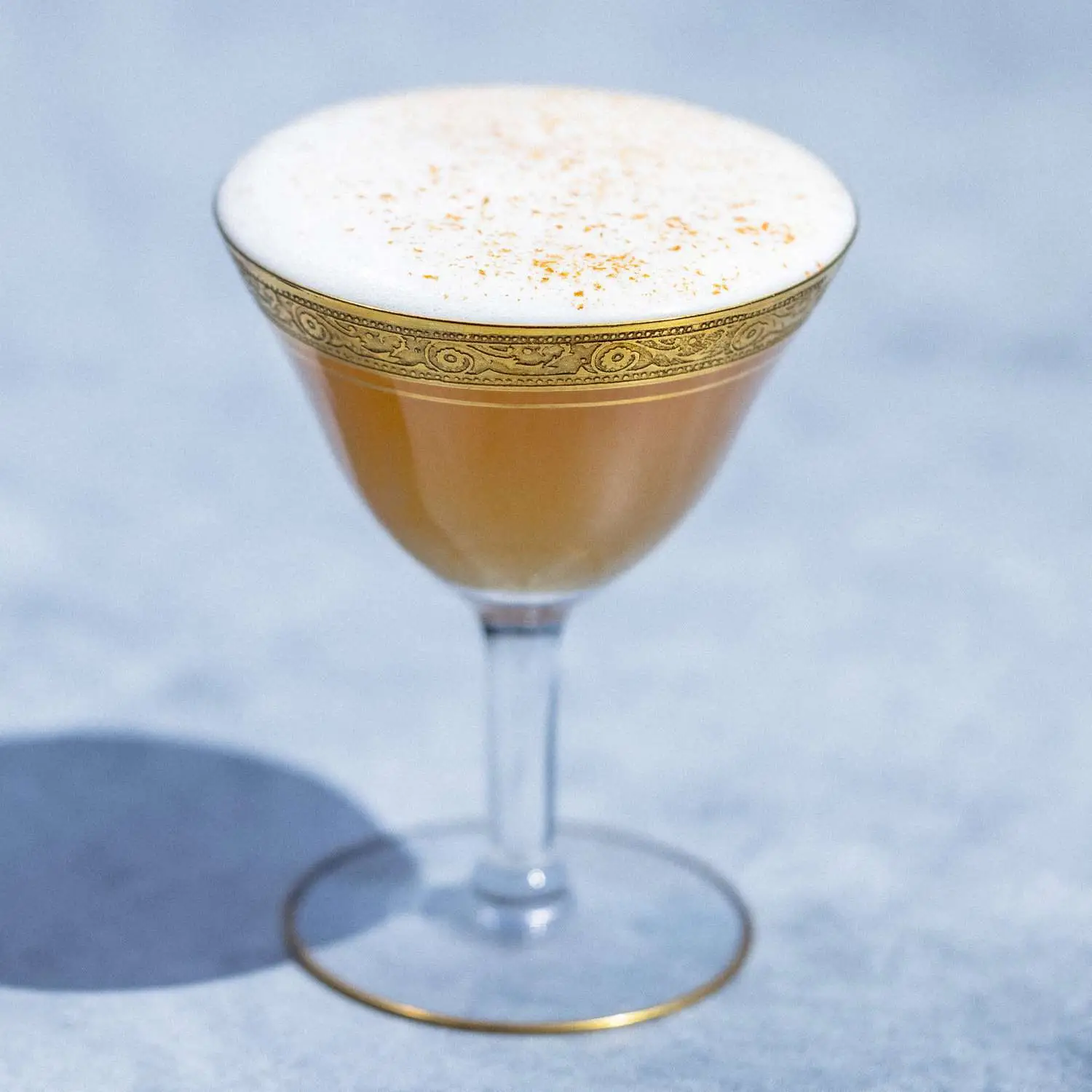 Smoke Show mezcal cocktail with foam on top, served in ornate gold-trimmed coupe glass and garnished with cinnamon