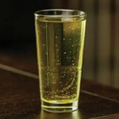 A tall pint glass holds a pale yellow sparkling drink with no ice. 