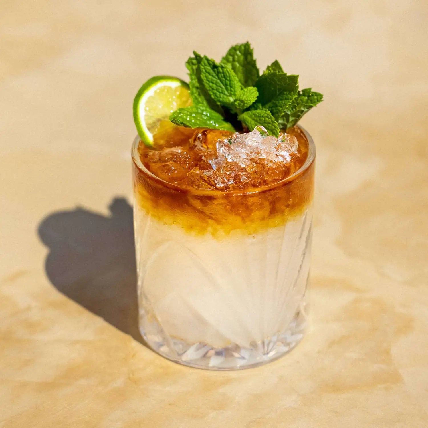 Mai Tai in rocks glass with rum float, crushed ice, mint sprigs and lime wheel shot on tan surface