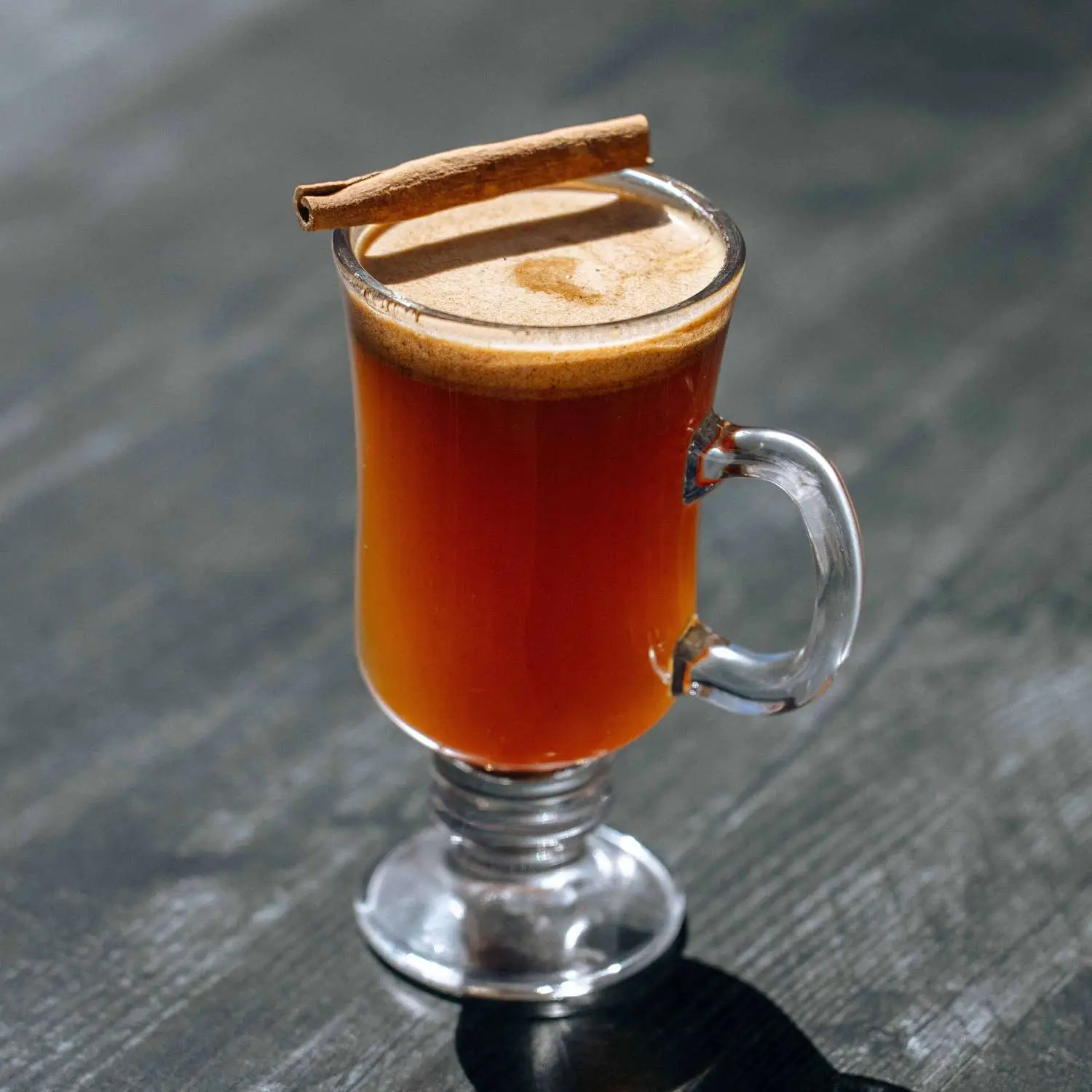 Hot Caramel Buttered Rum in clear, footed mug, with cinnamon stick garnish