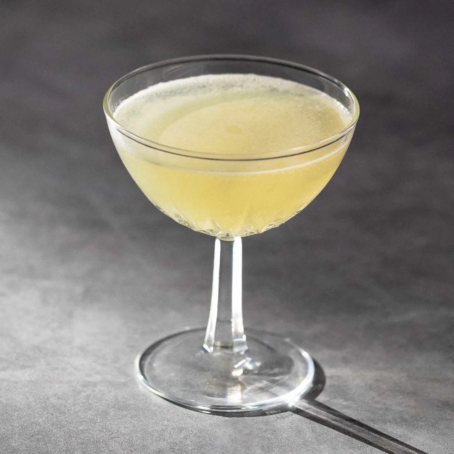 Mezcal Last Word in coupe glass with v-shaped etching, on marble background