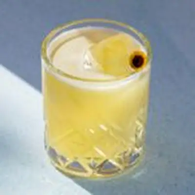 A soft yellow cocktail in a rocks glass garnished with a Szechuan button