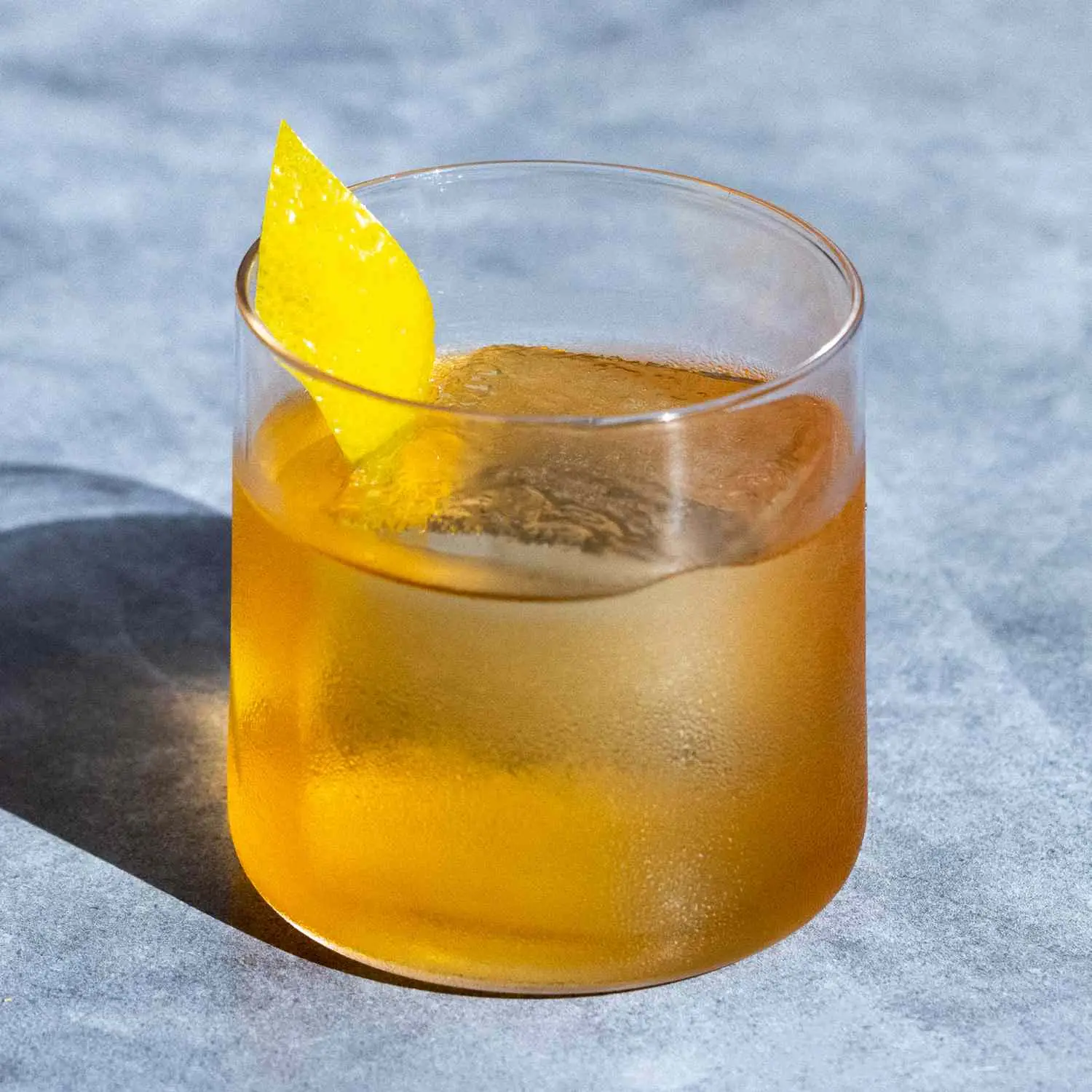 Rusty Nail cocktail in a rocks glass with single large ice cube and lemon twist garnish