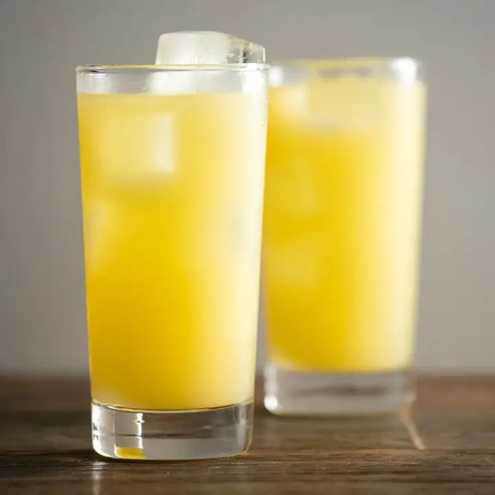 two bright-yellow gin and juice cocktails on a wooden bar