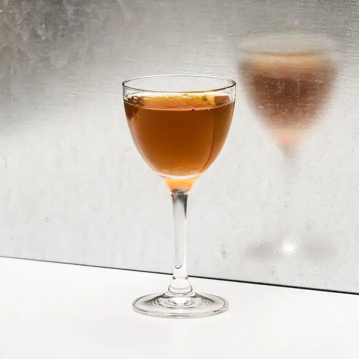 nail in the coffin cocktail in a Nick & Nora glass, set against a reflective wall