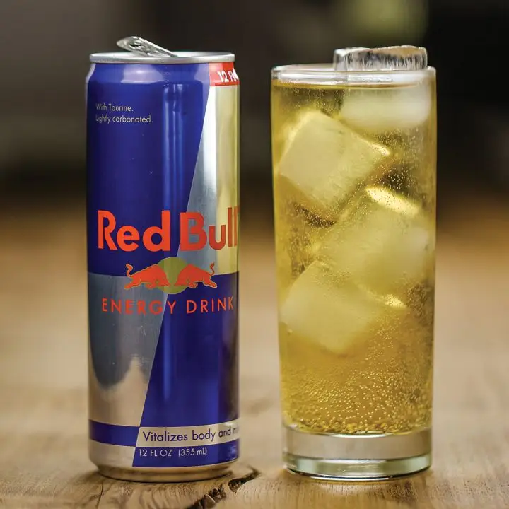 Vodka Red Bull in a glass with ice next to a can of Red Bull