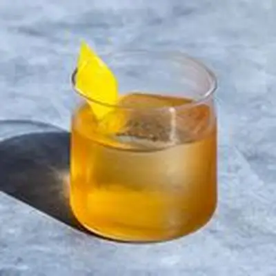 Rusty Nail cocktail in a rocks glass with single large ice cube and lemon twist garnish