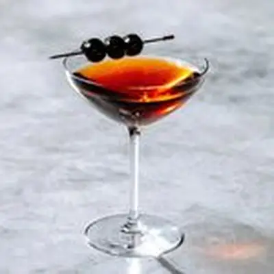 Rob Roy cocktail in coupe glass with three brandied cherries, shot on gray marble surface