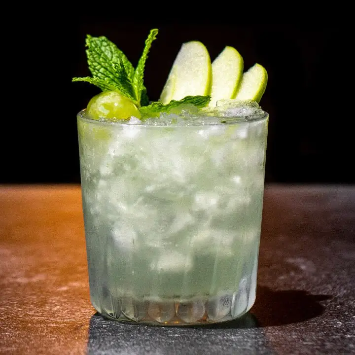 Space Gin Smash cocktail in a rocks glass over cracked ice, with green apple, green grape and mint garnishes