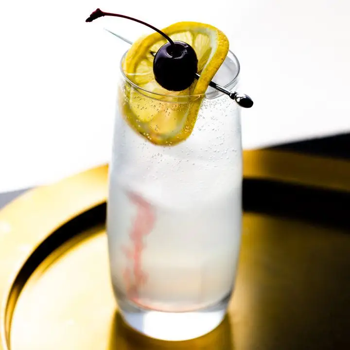 Tom Collins cocktail garnished with lemon wheel and maraschino cherry