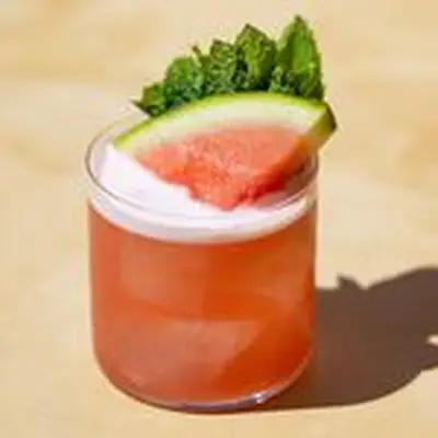 Red-pink watermelon Margarita in a rocks glass with watermelon wedge and mint spring garnish on top