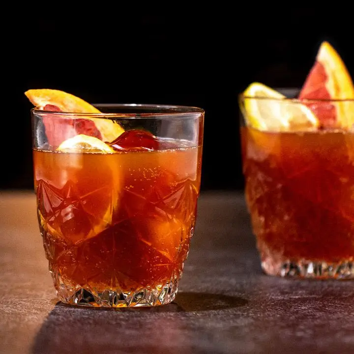 Two short punch glasses with intricate inlays rest on a granite bar top. They