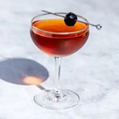 Manhattan cocktail in a curved coupe glass, with maraschino cherry garnish on a metal cocktail skewer