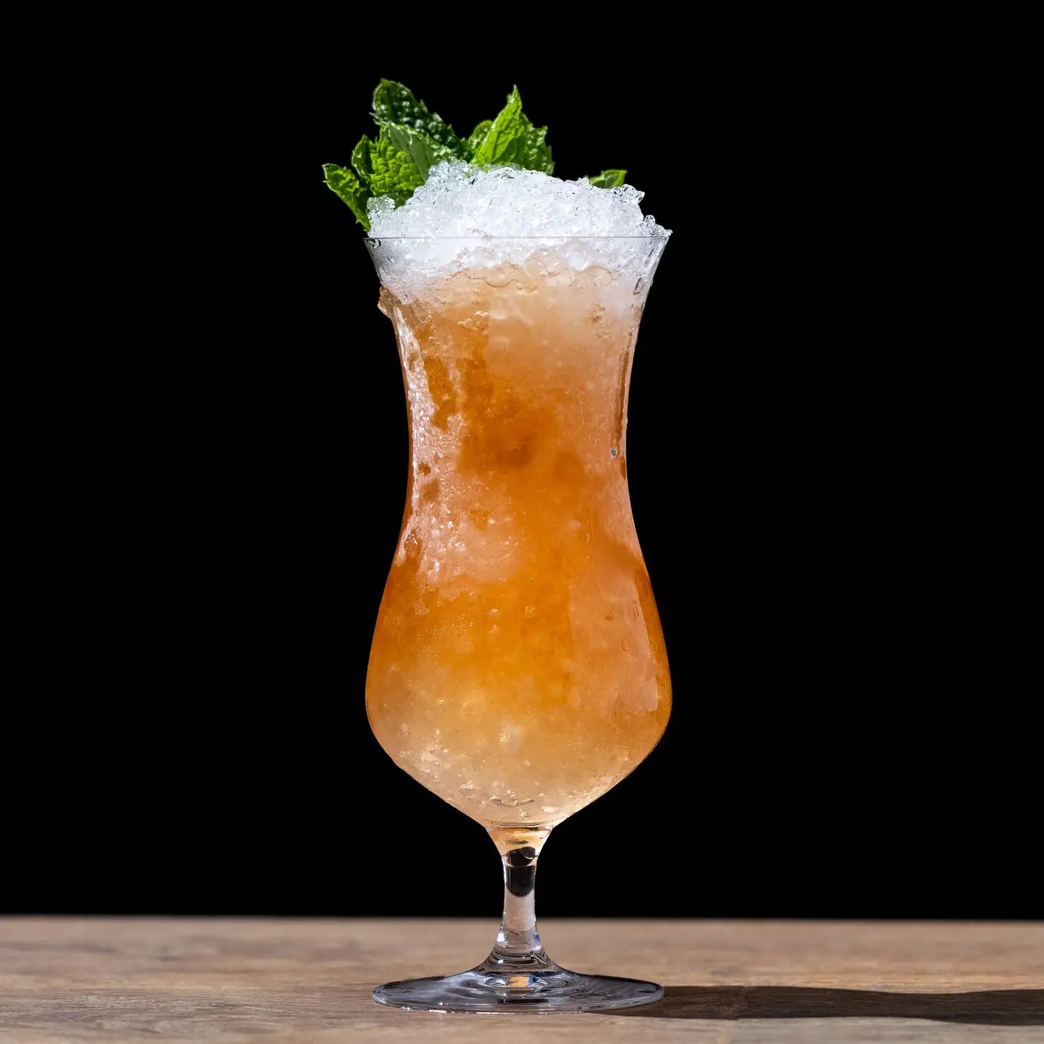 Zombie cocktail in curved Hurricane glass, orange hued over crushed ice with mint sprig garnish, on back background