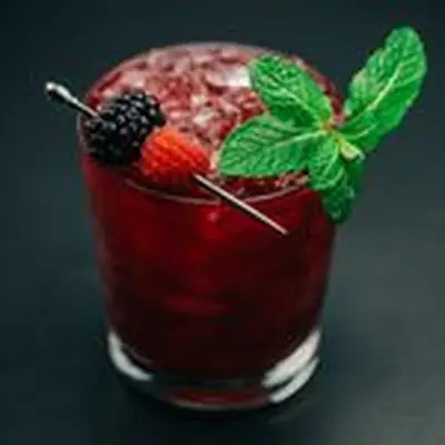 A deep purple cocktail over crushed ice in a rocks glass garnished with skewered berries and a mint sprig