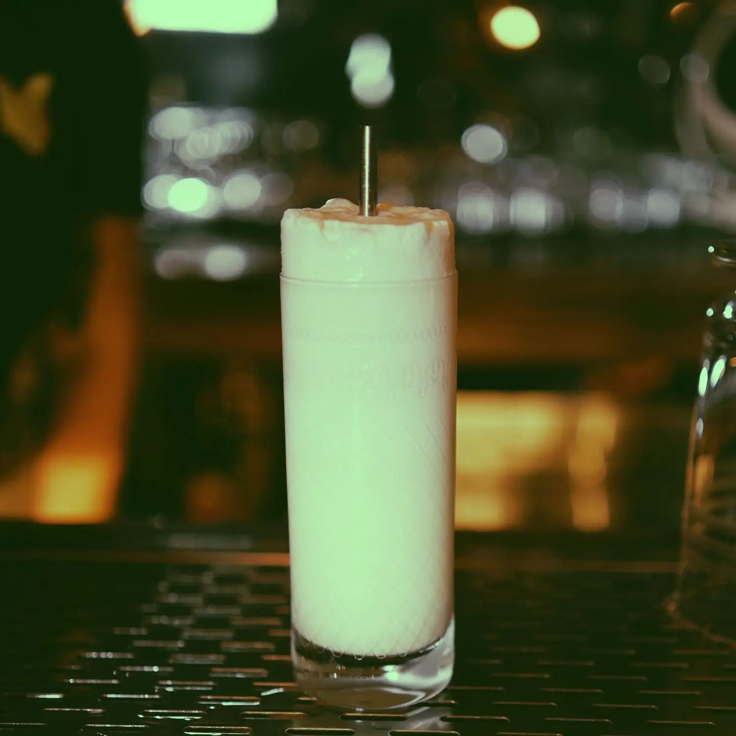 Ramos Melon Fizz cocktail with heavy foam and metal straw, shot in Collins glass on bar grate