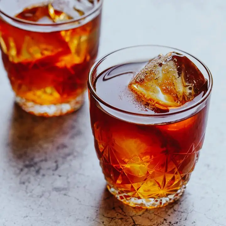 Two rocks glasses with star-like designs hold a crimson drink over a few large ice cubes. They’re dusted with nutmeg. 