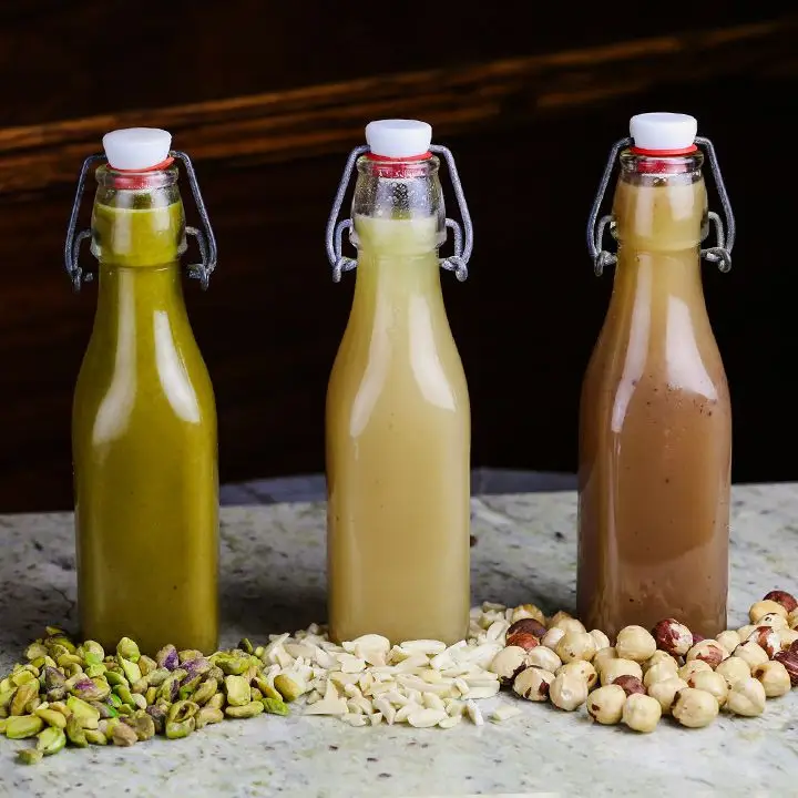 three swing-top bottles of orgeat (pistachio, almond and hazelnut) sitting behind piles of nuts