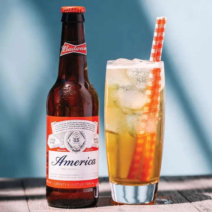 Big Red cocktail in a Collins glass over ice with two red-and-white straws, served next to a bottle of Budweiser