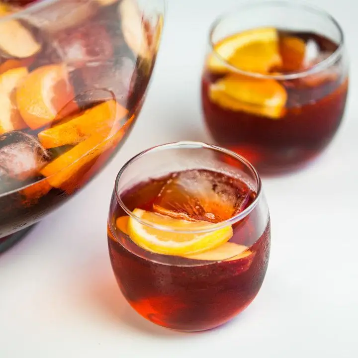 Negroni Sbagliato in a punch bowl and two serving glasses, topped with fresh orange slices