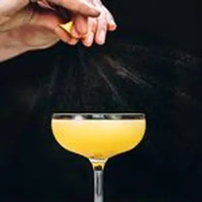 hands express lemon peel oils over the Applejack Rabbit cocktail, served in a coupe glass